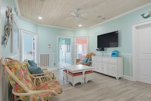 A room with a ceiling fan, a television, a dining table, wicker furniture, and a white cabinet. - Oceanfront with hot tub and elevator (North Topsail Beach)