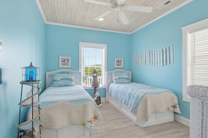 A bedroom with two beds, a ceiling fan, a window with a view, and a wall-mounted decoration. - Oceanfront with hot tub and elevator (North Topsail Beach)