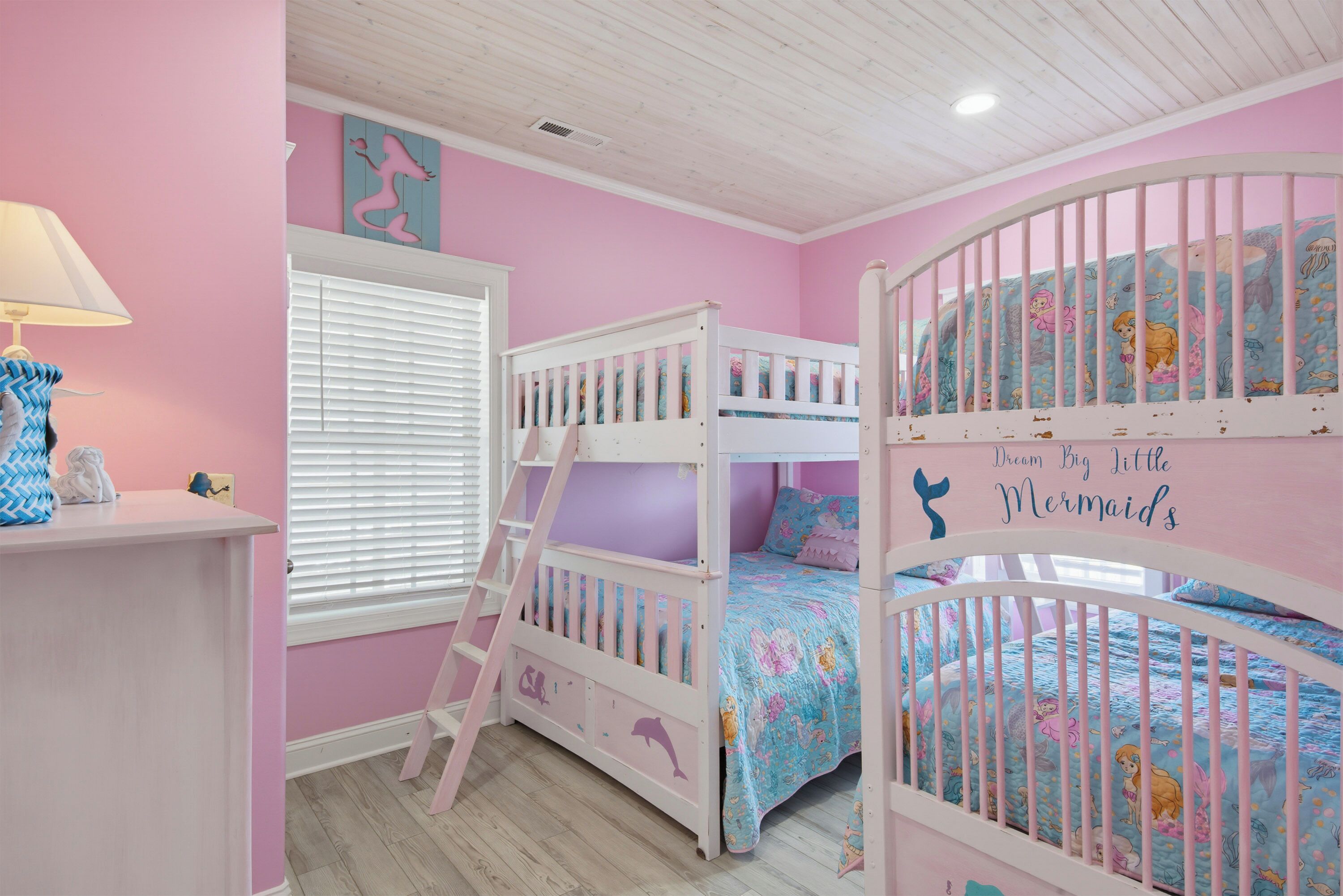 A child's bedroom with bunk beds, a window with blinds, and a wall with a mermaid decal.