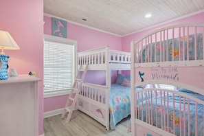 A child's bedroom with bunk beds, a window with blinds, and a wall with a mermaid decal. - Oceanfront with hot tub and elevator (North Topsail Beach)