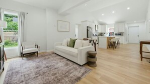 A spacious living area with a white sofa, a coffee table, and a view of the kitchen in the background. - Modern West End Home | BeltLine/Downtown Access (Atlanta)