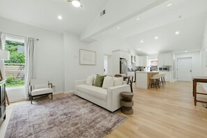 A spacious living area with a white sofa, a coffee table, and a view of the kitchen in the background. - Modern West End Home | BeltLine/Downtown Access (Atlanta)