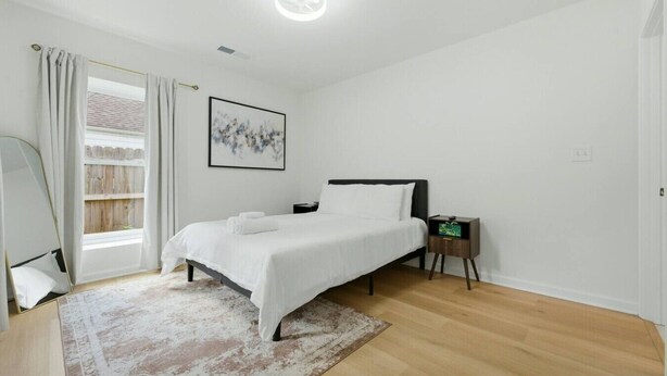 A bedroom with a bed, a bedside table, a rug, a window with curtains, and a wall-mounted picture. - Modern West End Home | BeltLine/Downtown Access (Atlanta)