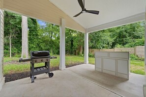 An outdoor patio with a grill and a built-in bar area, surrounded by trees. - Modern West End Home | BeltLine/Downtown Access (Atlanta)