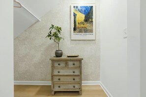 A room with a textured wall, a wooden dresser with drawers, a potted plant, and a framed artwork of a street scene. - West End Gem | Near Mercedes-Benz Stadium, Pet OK (Atlanta)