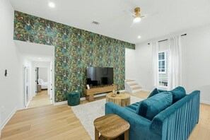 Ein modernes Wohnzimmer mit Flachbildfernseher, einem blauen Sofa, einem Holztisch und einer Wand mit Muster.