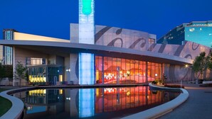 Ein modernes Gebäude mit großer Glasfassade, einer zentralen vertikalen Struktur und einem reflektierenden Wasserspiel davor.