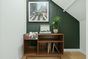 A room with a wooden console table, a framed picture, a turntable, and a potted plant. - Atlanta West End Getaway | Near BeltLine/Downtown (Atlanta)