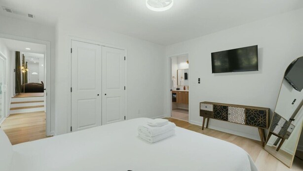 Habitación de hotel con cama, mesita de noche, televisor montado en la pared y puerta que da a un baño.