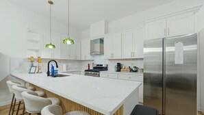 Cocina moderna con armarios blancos, una isla central con taburetes y un refrigerador de acero inoxidable, además de una estufa a gas.