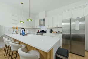 A modern kitchen with white cabinetry, a central island with bar stools, a stainless steel refrigerator, and a gas stove. - Atlanta West End Getaway | Near BeltLine/Downtown (Atlanta)