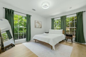 Ein Schlafzimmer mit einem Bett, einem Nachttisch, einem Sessel und einem Fenster mit Vorhängen.