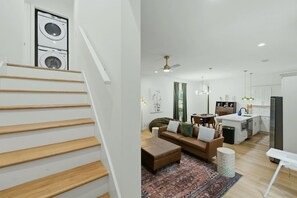En modern lägenhet med en trappa, ett vardagsrum med soffa och soffbord, ett kök med kylskåp och en tvättmaskin i hörnet.