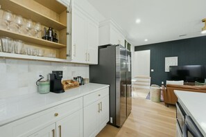 Une cuisine moderne avec des meubles blancs, un réfrigérateur en acier inoxydable et un coin café.
