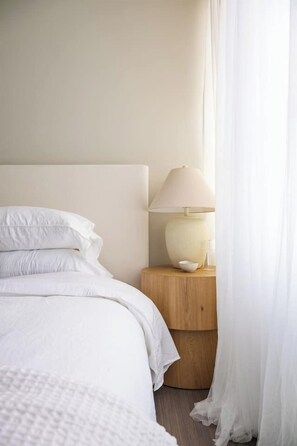 Un lit bien fait, avec une literie blanche, une lampe de chevet et une table de chevet en bois.
