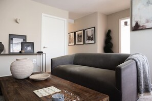 A living room with a grey sofa, a wooden coffee table with decorative items, and framed pictures on the wall. - Gracious 2 Bed 2 Bath Apartment with Free Parking (Arlington)