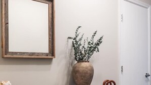 A reception desk with a wooden finish, a large mirror, a potted plant, a small stone, and a black bag. - Gracious 2 Bed 2 Bath Apartment with Free Parking (Arlington)