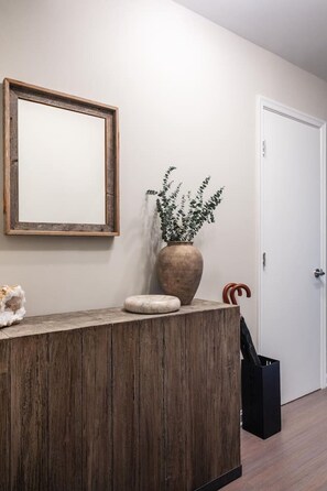 A reception desk with a wooden finish, a large mirror, a potted plant, a small stone, and a black bag. - Gracious 2 Bed 2 Bath Apartment with Free Parking (Arlington)