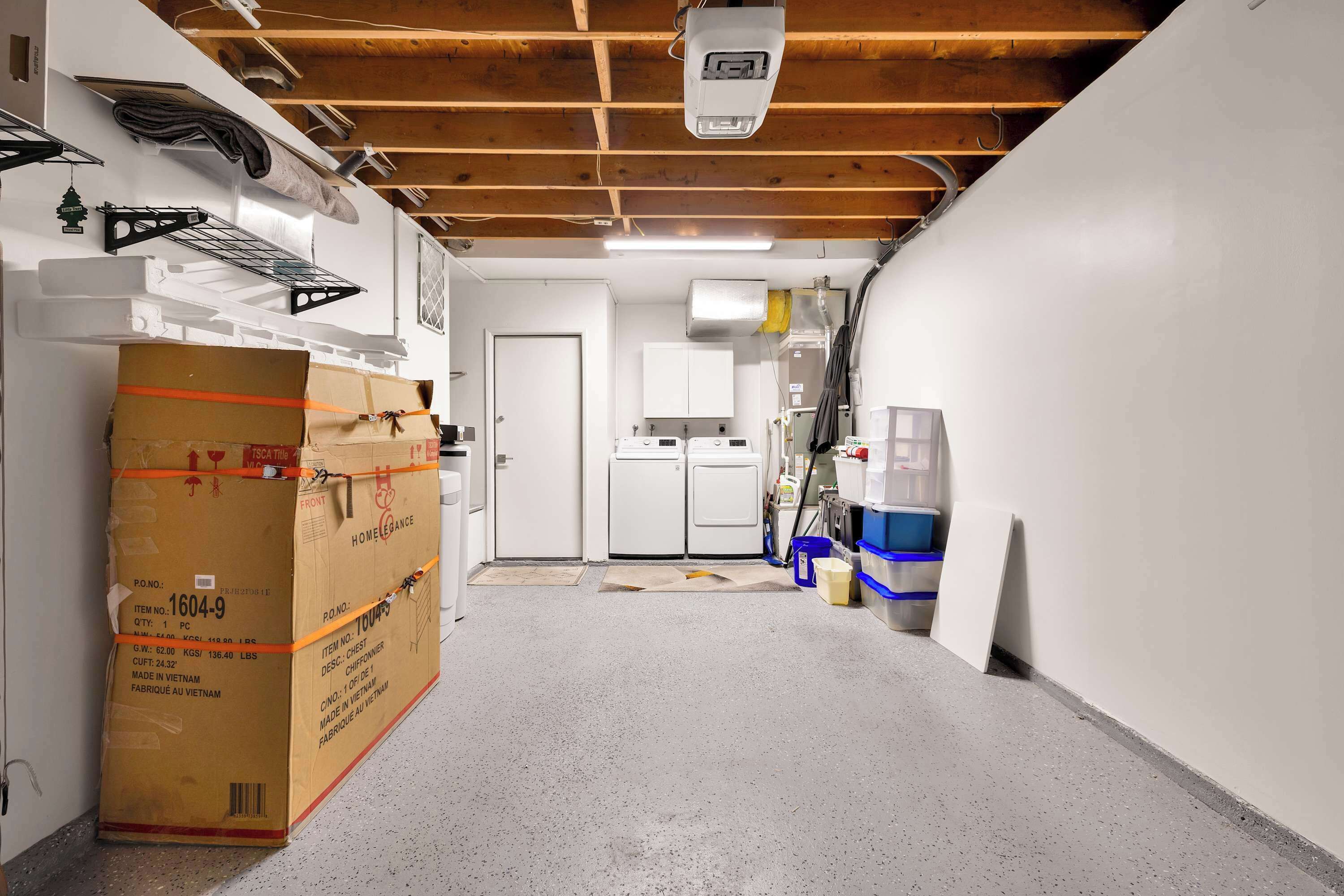 Un couloir étroit avec un grand carton, une porte blanche et un lave-linge blanc.