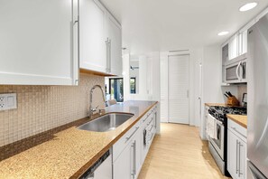 A modern kitchen with white cabinets, a granite countertop, stainless steel appliances, and a tiled backsplash. - Rose Garden Escape - Stylish 2 Bedroom Condo (Palm Springs)