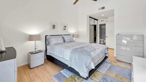 Ein Schlafzimmer mit einem Bett, Nachttischen, einem Schminktisch, einem Deckenventilator und einer Tür zu einem Badezimmer.