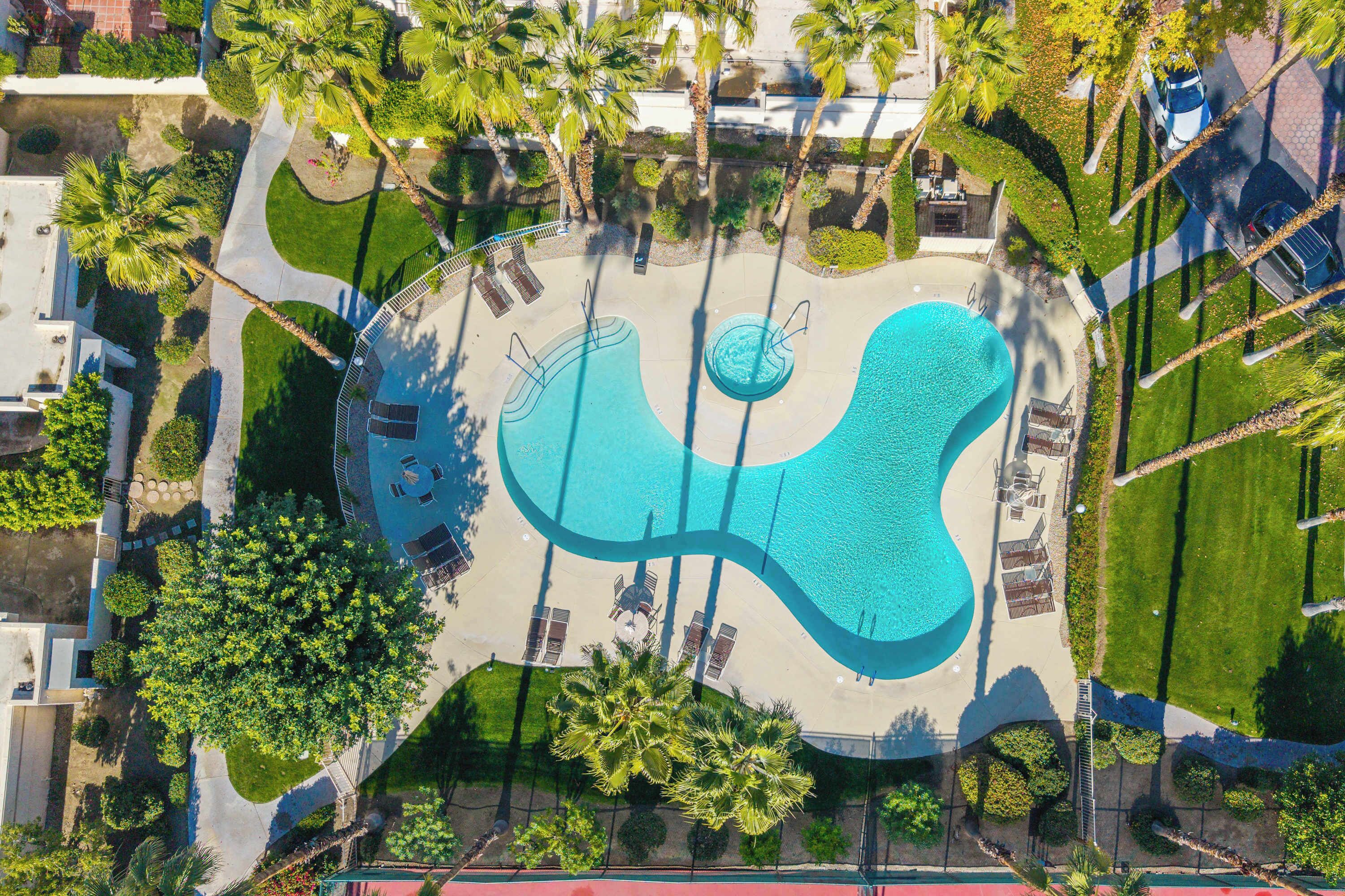 An aerial view of a pool area with multiple swimming pools, sun loungers, and surrounding greenery.
