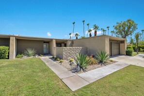 A two-story house with a stone accent wall, a front lawn, and a variety of desert plants. - Rose Garden Escape - Stylish 2 Bedroom Condo (Palm Springs)