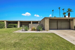 A residential property with a garage, a well-maintained lawn, and a clear blue sky. - Rose Garden Escape - Stylish 2 Bedroom Condo (Palm Springs)
