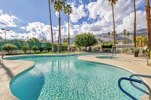 A swimming pool with clear water, surrounded by palm trees and a mountain backdrop. - Rose Garden Escape - Stylish 2 Bedroom Condo (Palm Springs)