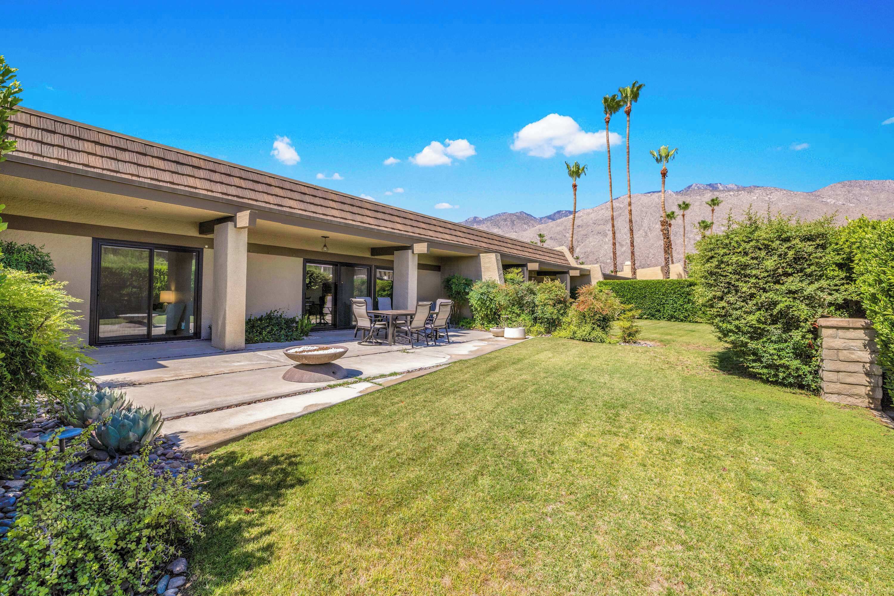 Una casa moderna con un patio, mobiliario exterior y un césped cuidado.