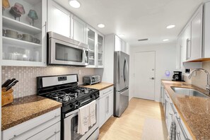 A modern kitchen with white cabinetry, stainless steel appliances, a granite countertop, and a tiled backsplash. - Rose Garden Escape - Stylish 2 Bedroom Condo (Palm Springs)