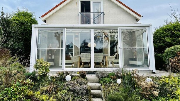 Et moderne hus med et drivhus af glas, rødt tag og en have med forskellige planter.