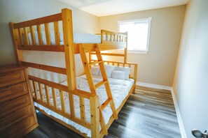 A bunk bed with a wooden frame and white bedding in a room with wooden flooring and a window.