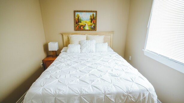 A neatly made bed with a white duvet, a wooden headboard, and a bedside table with a lamp.