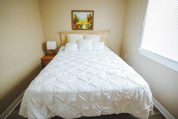 A neatly made bed with a white duvet, a wooden headboard, and a bedside table with a lamp.