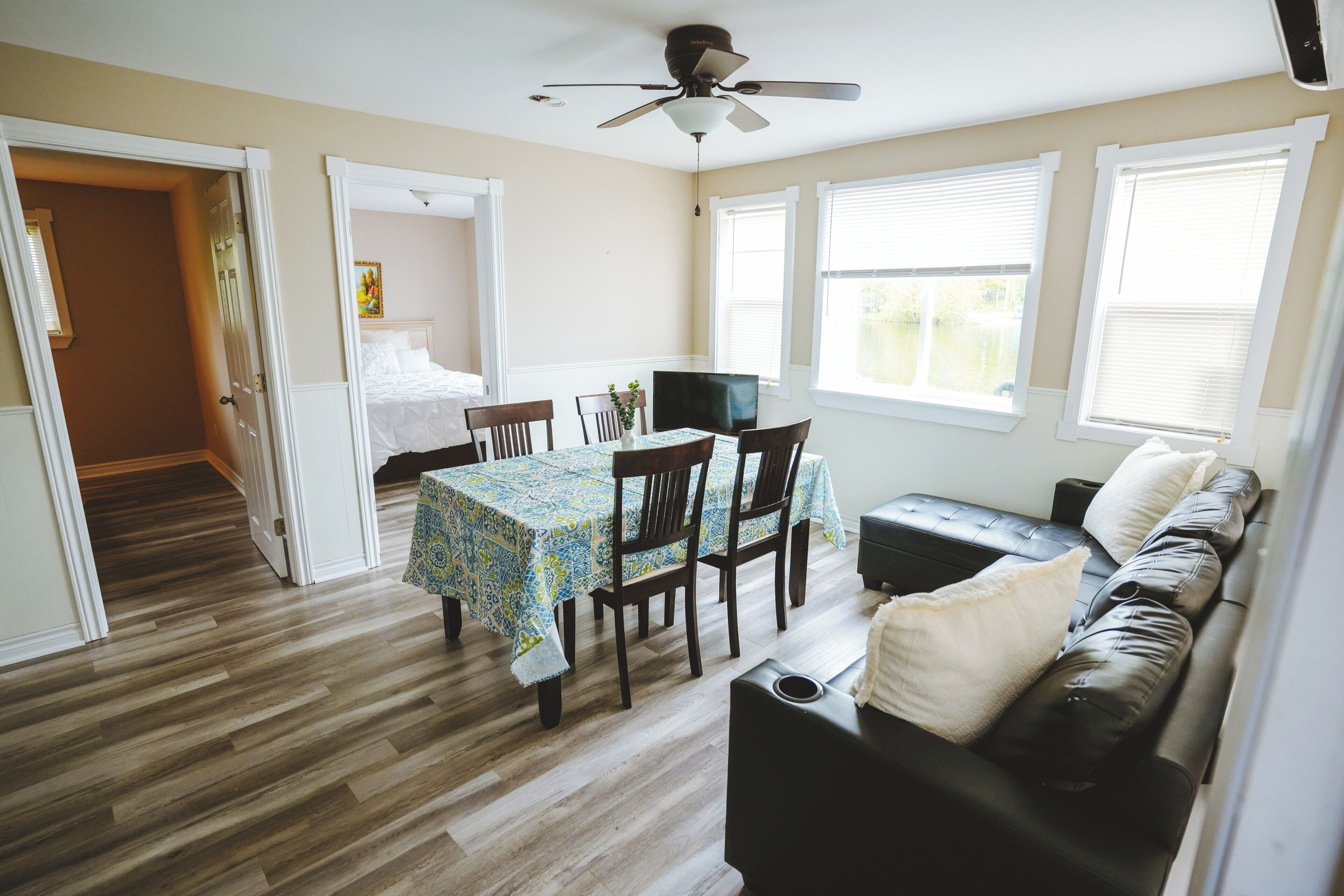 Une pièce comprenant une table à manger, des chaises, un canapé en cuir noir, un ventilateur de plafond et une fenêtre avec des stores.