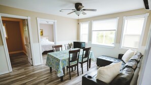 A room with a dining table, chairs, a black leather sofa, a ceiling fan, and a window with blinds.