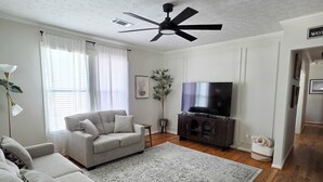 Ein Wohnzimmer mit einer Couch, einem Couchtisch, einem Fernseher und einem Deckenventilator.