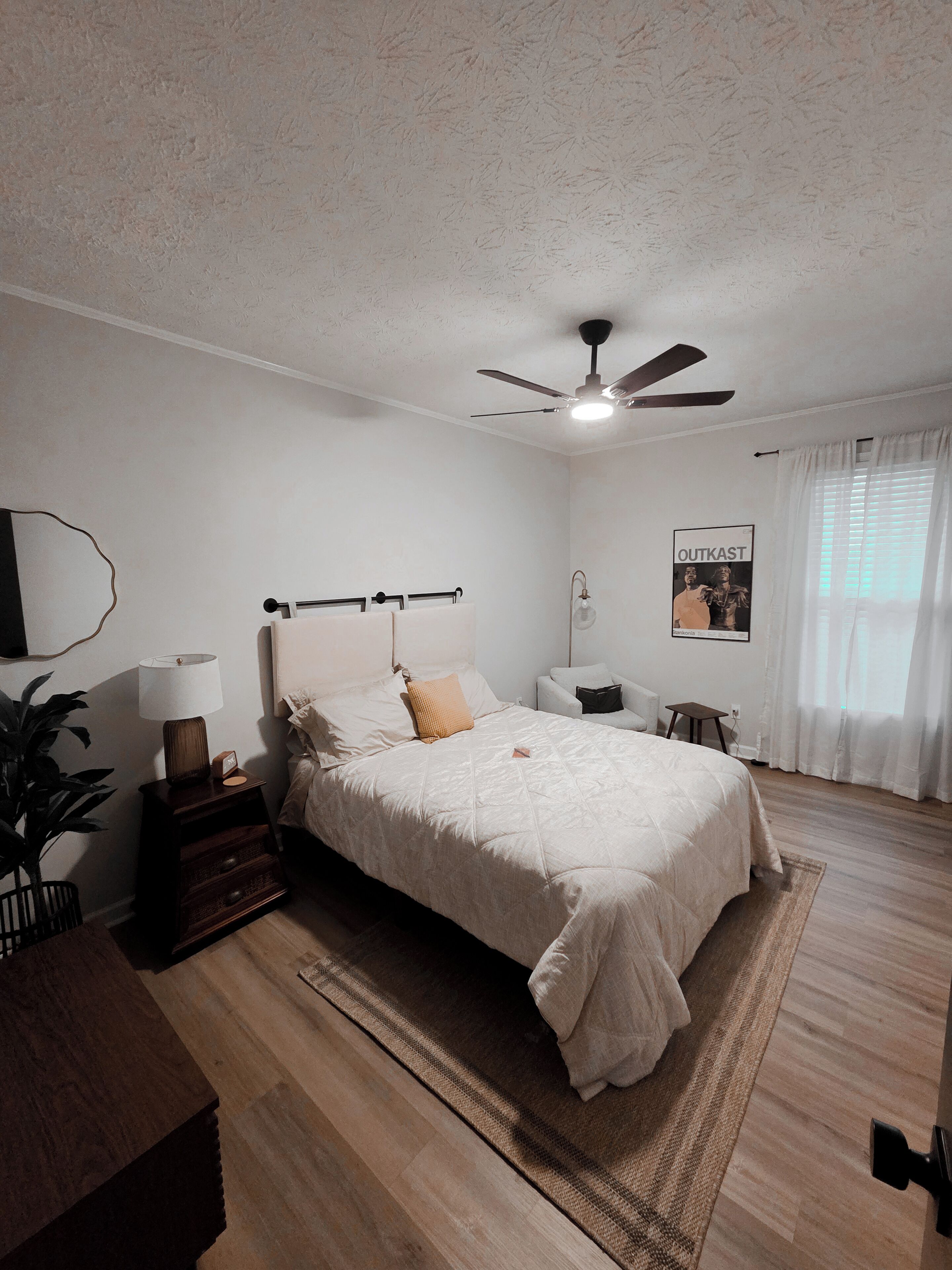 A bedroom with a bed, bedside tables, a ceiling fan, a poster on the wall, and a window with curtains.