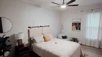 A bedroom with a bed, bedside tables, a ceiling fan, a poster on the wall, and a window with curtains.