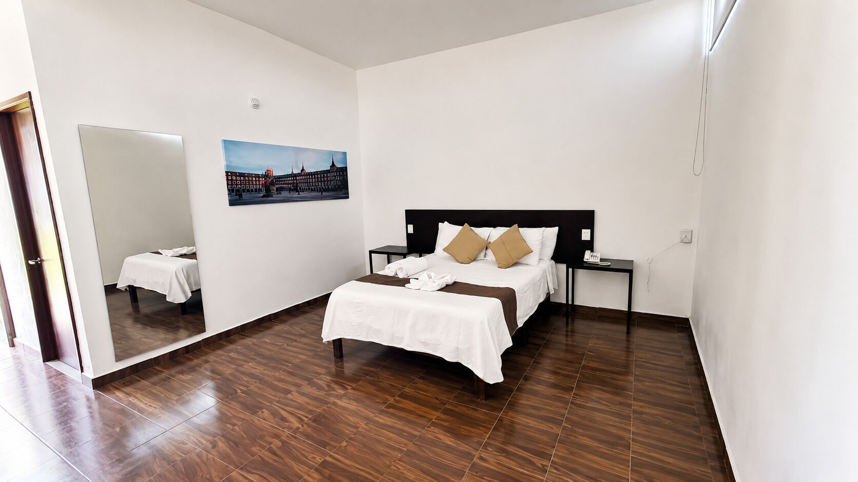 Ein Hotelzimmer mit einem Bett, einem Nachttisch, einem Spiegel und einem an der Wand hängenden Bild.