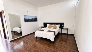 Una habitación de hotel con cama, mesita de noche, espejo y un cuadro colgado en la pared.