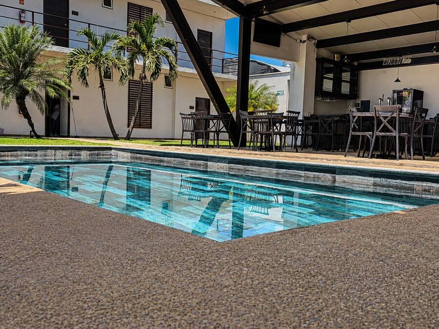 Una piscina con borde de baldosas, rodeada de mobiliario de exterior y palmeras.