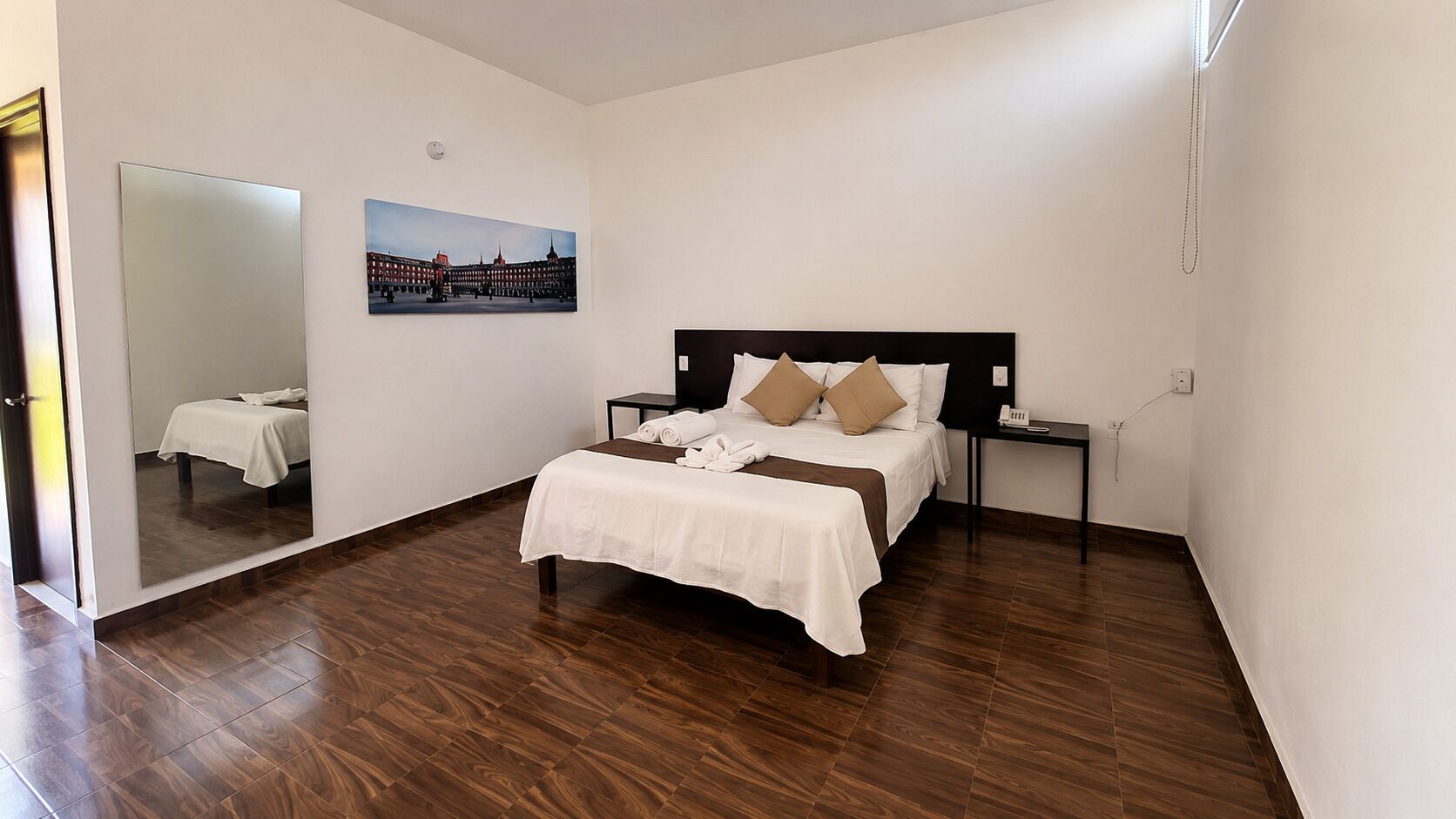 Een hotelkamer met een bed, nachtkastjes, een spiegel en een schilderij aan de muur.