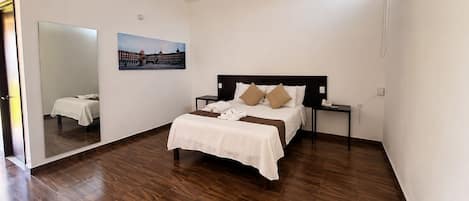 A hotel room with a bed, bedside tables, a mirror, and a wall-mounted painting.