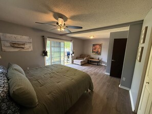 A bedroom with a bed, a ceiling fan, a sliding glass door leading to a patio, and a door to another room. - The Nautical City Nook (Rogers City)