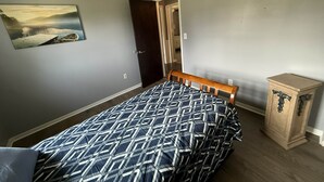 Un dormitorio con una cama, un banco de madera, un mueble pequeño y un cuadro en la pared.
