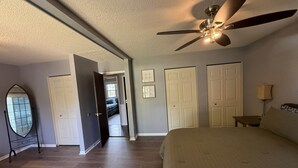 A bedroom with a bed, a ceiling fan, a mirror, and a door leading to another room.