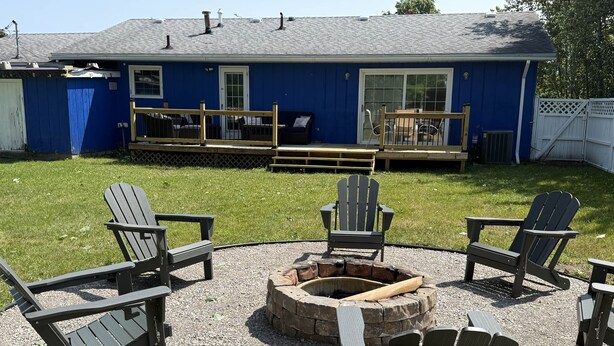 Un patio trasero con una chimenea, sillas Adirondack y una casa azul.