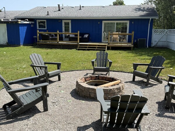 A backyard with a fire pit, Adirondack chairs, and a blue house.